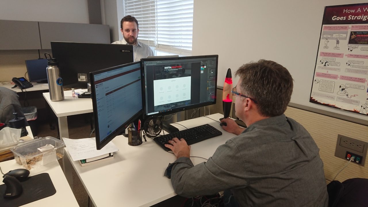 Sandbox team member, Jim, works at his desk designing a website. He has two monitors set up on his desk while working.